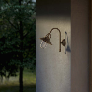 Outdoor brass wall lamp with curved arm protective hood and transparent glass diffuser rustic style Giada collection by Ghidini 1849 - Finish: OBM Bronze Satin Matt Brass