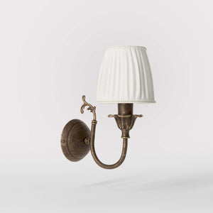 Classic brass wall lamp with pleated ivory white shade, decorative arm and floral details for elegant wall lighting - Finish: OAS Antique Brass