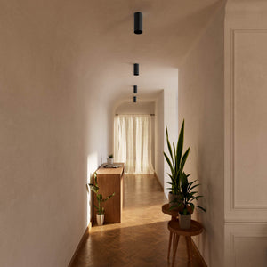 Cylinder ceiling lamp in brass with compact body installed on the ceiling of an elegant corridor by Ghidini 1849 - Finish: ONO Matt Black