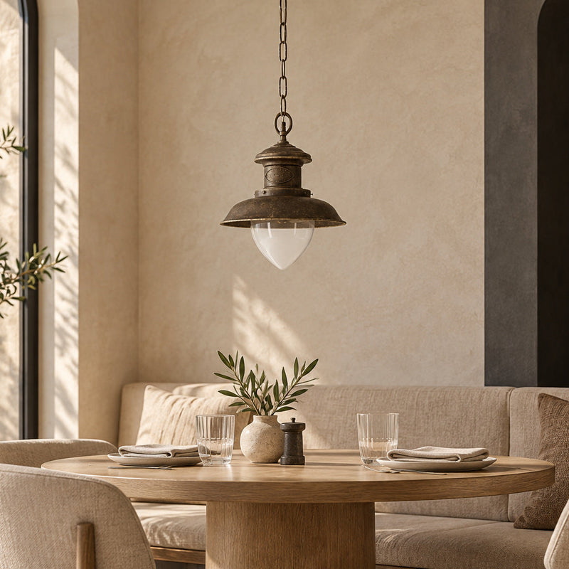 Suspension Al Mare à coupole en laiton foncé et verre transparent en goutte, au-dessus d’une table ronde.