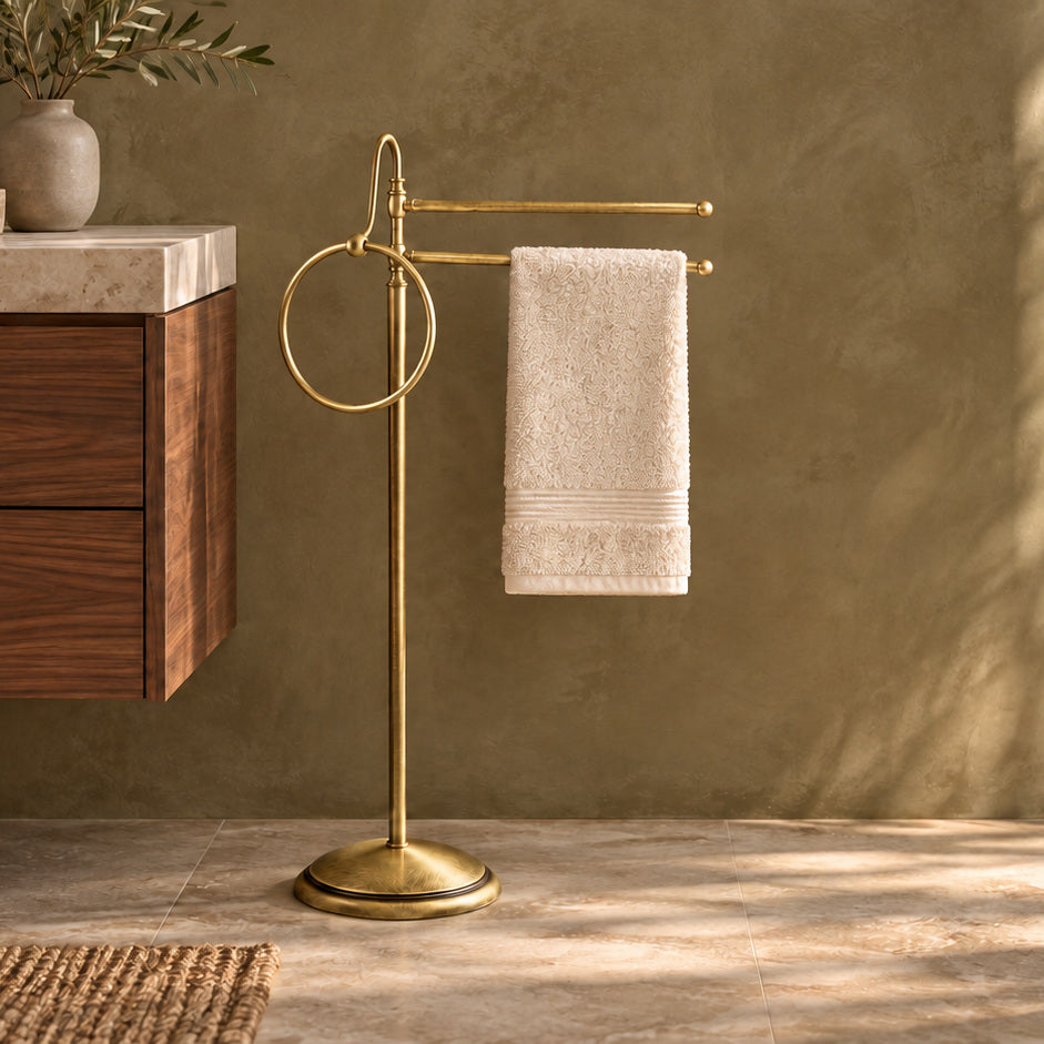 Porte-serviettes sur pied Alba en laiton bronze satiné, à deux barres mobiles et un anneau, près d’un meuble de salle de bains en noyer au plan en pierre claire.