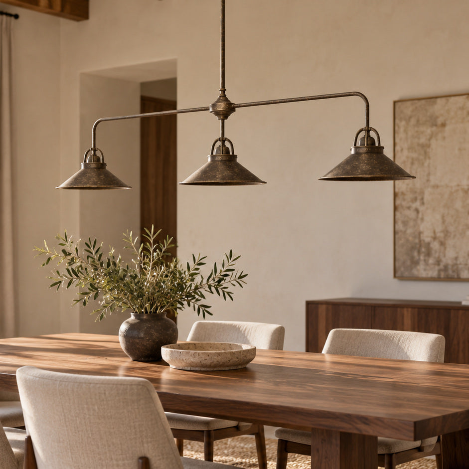Alice antique-brass pendant with three conical shades above a walnut dining table, both seen at a gentle angle.