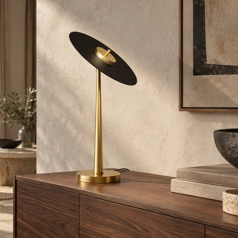 Lampe de table Anima en laiton et disque noir incliné sur un buffet en noyer
