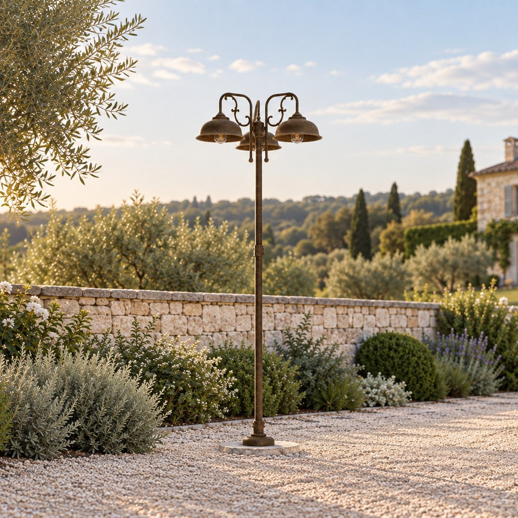 Lampadaire de jardin Lipari à trois lumières en laiton antique, près d'une allée de gravier et d'un mur de pierre