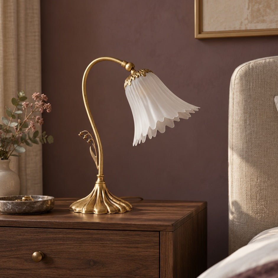 Lampe de table florale en laiton à finition bronze satinée, sur un chevet en noyer dans une chambre avec lit en lin.