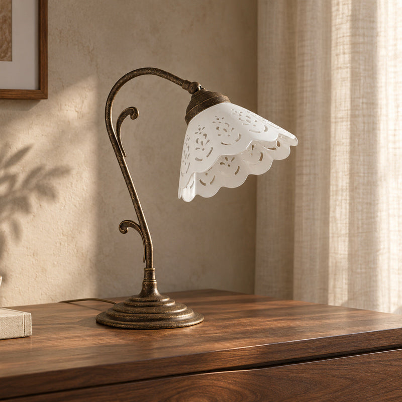 Lampada da tavolo Zefira in ottone anticato con paralume in ceramica bianca traforata su un mobile in noce.
