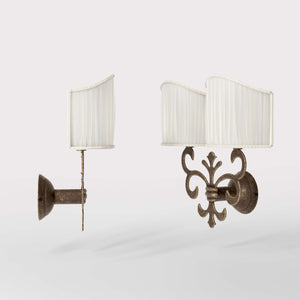 Neoclassical twin brass wall lamp with fleur-de-lis motif and symmetrical scrolls, white pleated shades, elegant Italian design - Finish: OAS Antique Brass