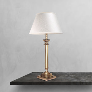 Brass table lamp with classic fabric shade in ivory white, decorative capital detail, ideal for elegant and timeless interiors