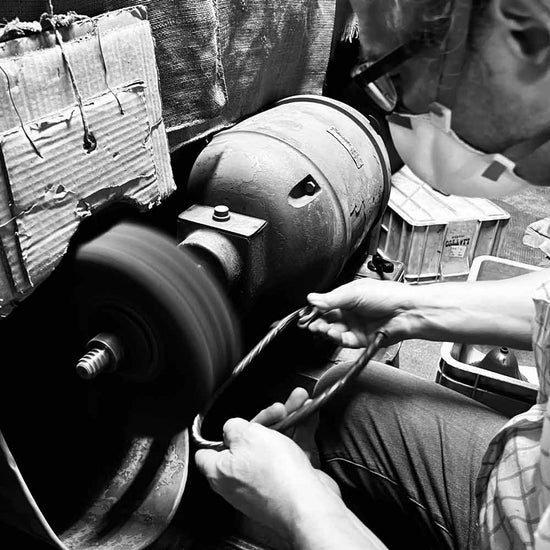 An artisan working the surface of a brass component at a finishing wheel