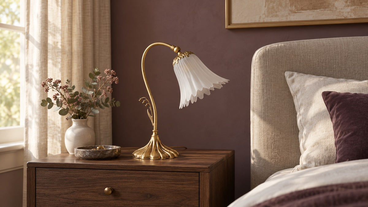 Lampe de table florale en laiton à finition bronze satinée, sur un chevet en noyer dans une chambre avec lit en lin.