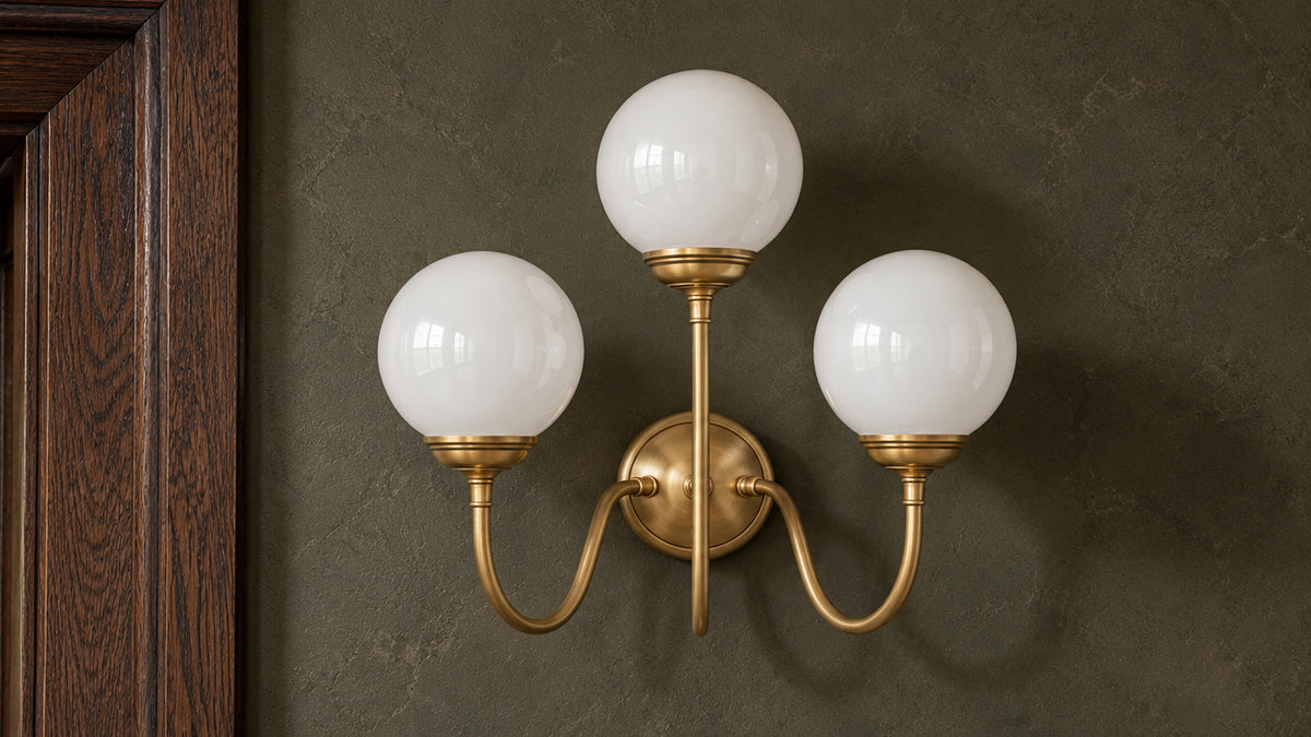 Incanto brass wall lamp with three glossy white globes beside a dark oak doorway.