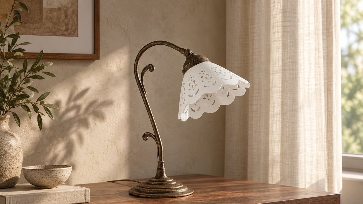 Lampada da tavolo Zefira in ottone anticato con paralume in ceramica bianca traforata su un mobile in noce.